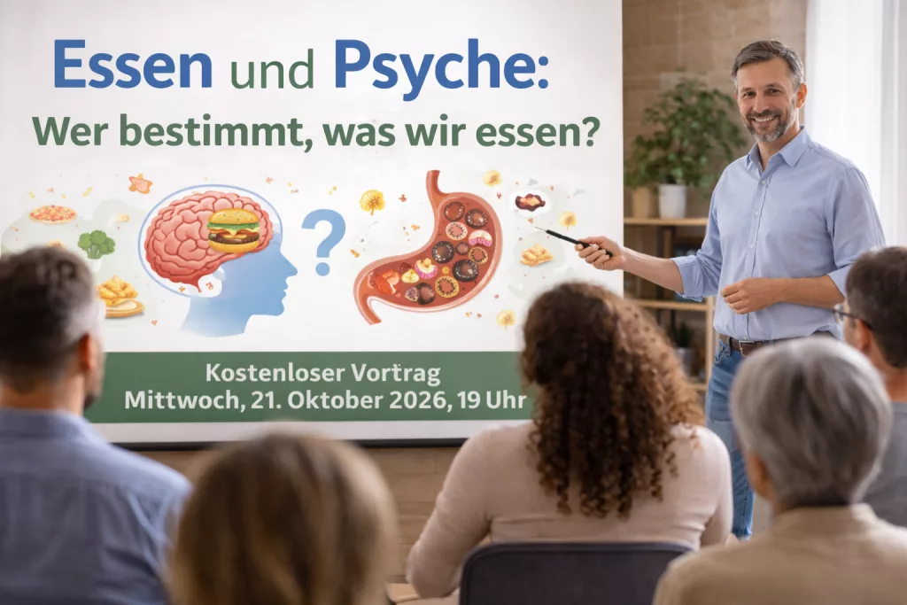 Ein Mann hält einen Vortrag und hat dabei ein großes Schaubild im Hintergrund. Stilisiert ist ein Kopf mit einem hervorgehobenem Hirn zu sehen, in dem ein Hamburger gezeichnet ist. Vor dem Kopf ein Fragezeichen. Daneben ist ein Magen abgebildet, der mit Pralinen gefüllt ist.